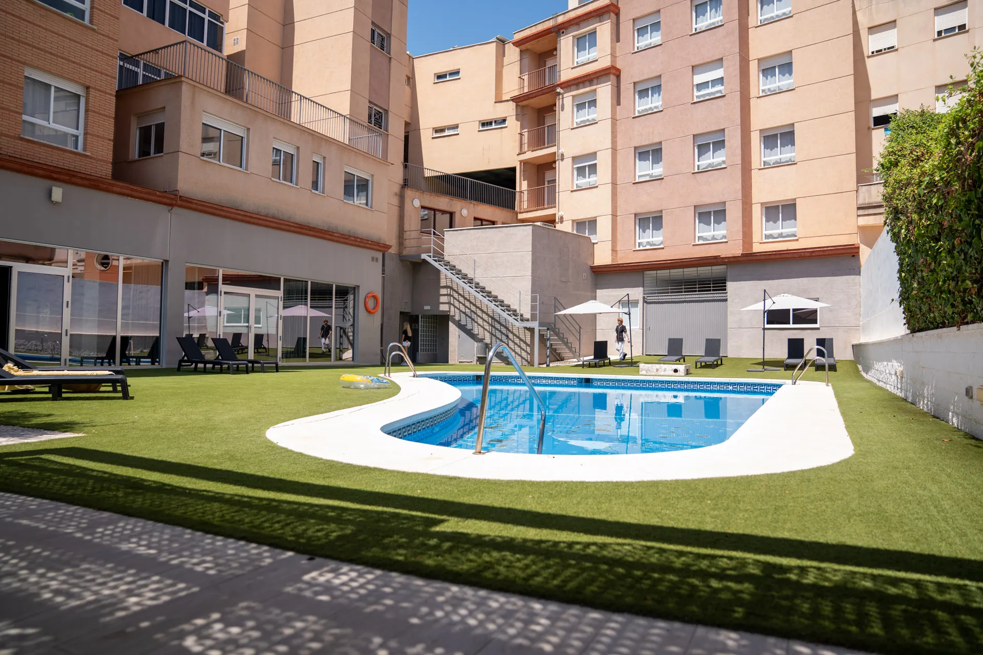 Vista amplia de la piscina de la residencia con el césped y el edificio al fondo